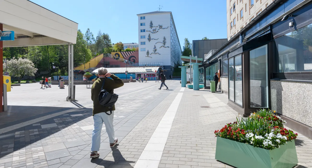 Vy över Hammarkulletorget. En man med ryggsäck går över torget. Flera personer i bakgrunden.