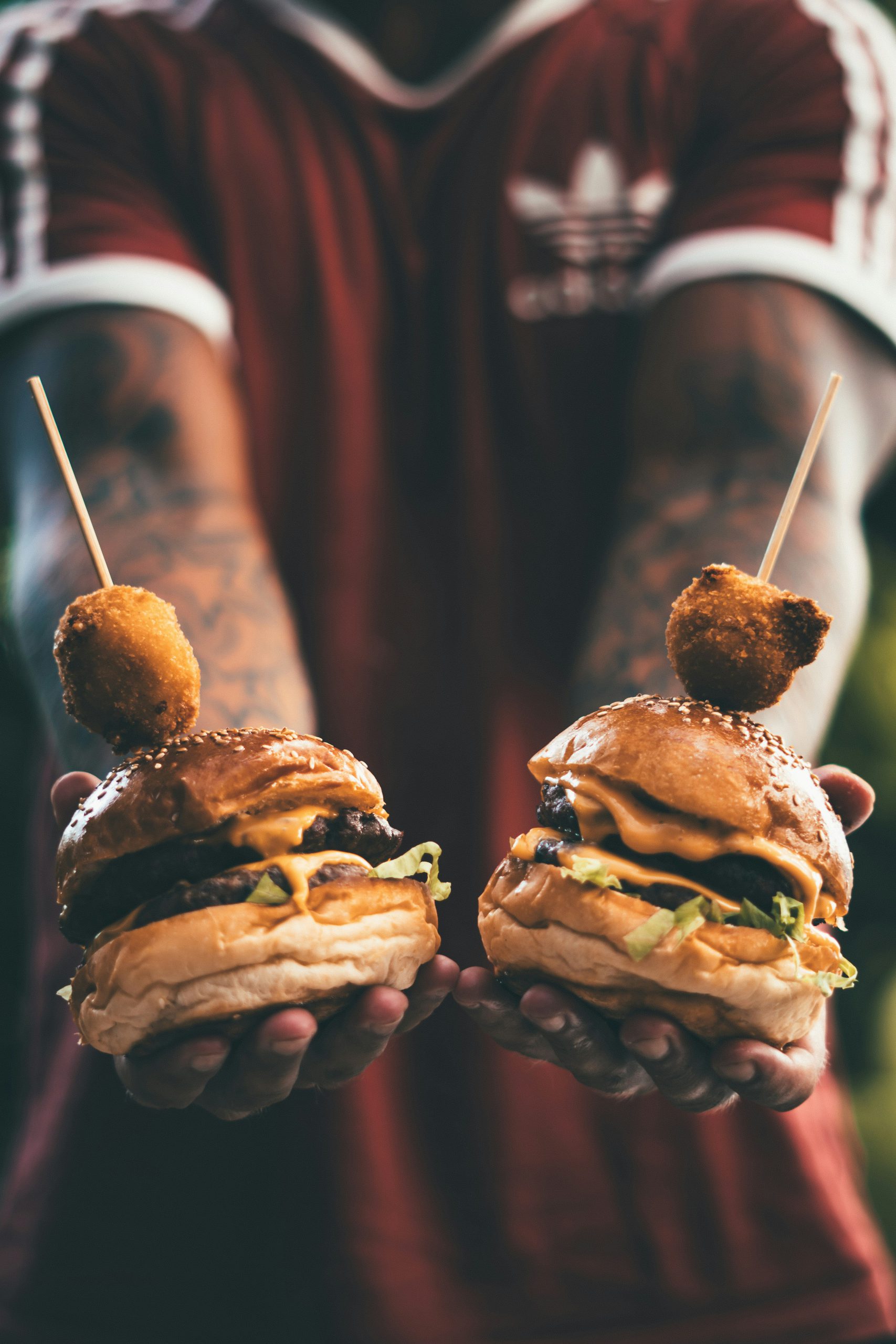 oliver-sjostrom-cff_w0ADWIA-unsplash Närbild på två hamburgare och två händer som håller i dom.